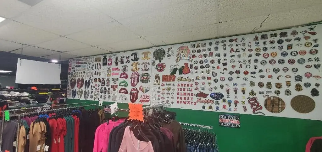 Wall of custom heat transfer patches and apparel racks inside the Fontz Graphics Designs shop